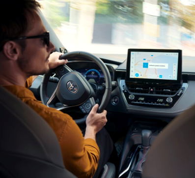 Un homme portant un pull orange effectue un virage à droite au volant de sa Toyota. Le système multimédia du véhicule affiche une mise à jour du logiciel.
