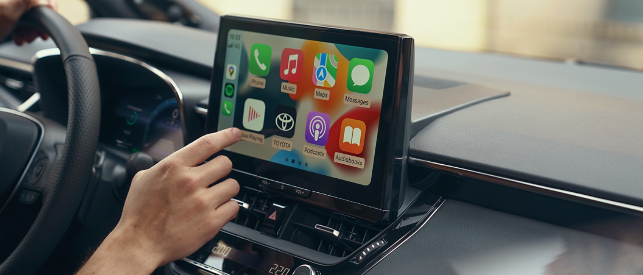 Une personne assise dans une Toyota utilise l’écran tactile multimédia. L’écran d’accueil Apple CarPlay s’affiche.