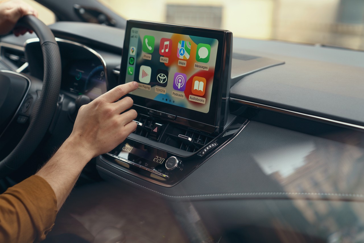 Une personne assise dans une Toyota utilise l’écran tactile multimédia. L’écran d’accueil Apple CarPlay s’affiche.