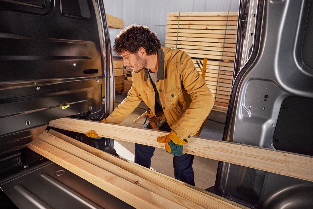 Un homme charge de longues planches de bois à bord du Proace